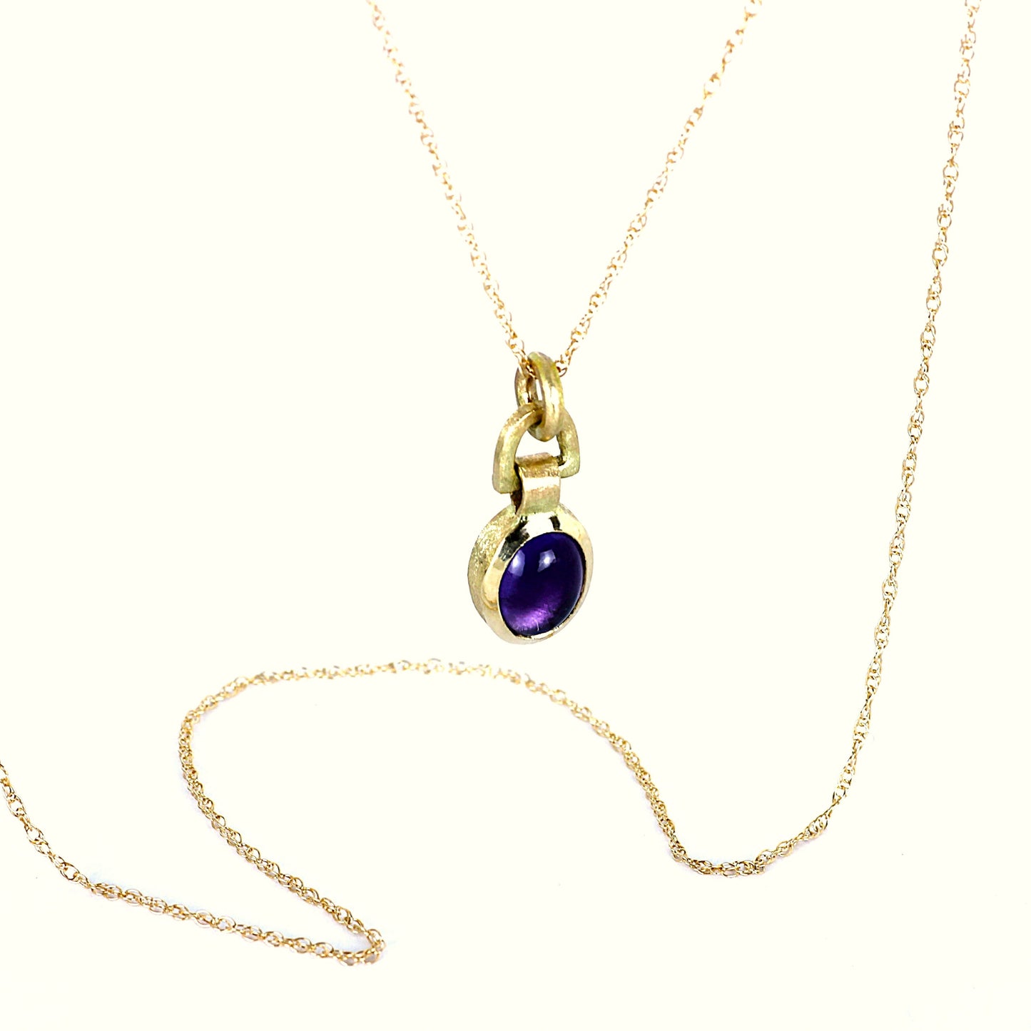 A gold chain necklace with a small gold pendant featuring a round purple gemstone, displayed on a clean white background.