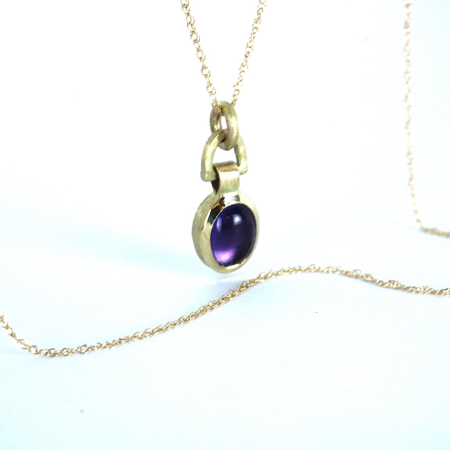 A gold necklace with a 8x6mm oval purple Amethyst gemstone pendant, displayed on a clean white background.