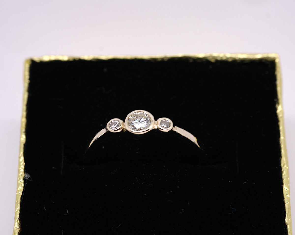 May include: A gold ring with three round diamonds. The center diamond is larger than the two diamonds on either side.